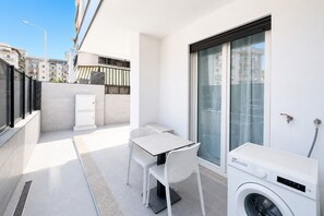 A compact balcony with a washing machine, a small table, and chairs. - GuestHost - Perla Nera Apartment 3 near the sea (Trani)