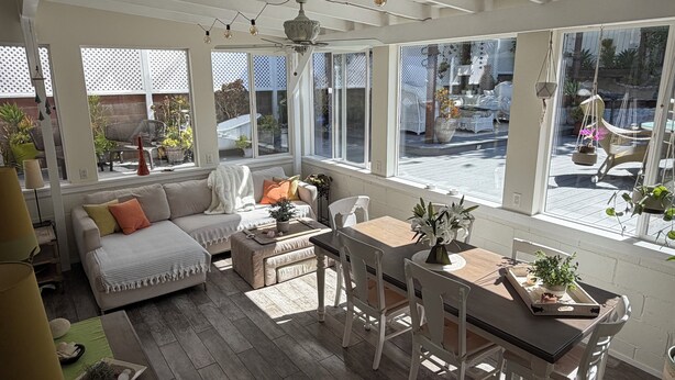 Et solbelyst rum med en sofa, et spisebord med stole og store vinduer.