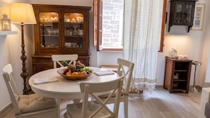 A dining area with a round table, white chairs, a fruit bowl, a wooden cabinet, and a lamp. - Albis 32 - Two Bedroom Apartment, Sleeps 4 (Alghero)