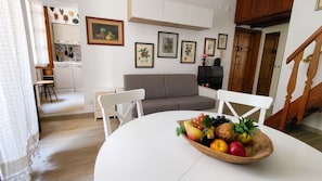 A modern living room with a dining table, a grey sofa, and a staircase. - Albis 32 - Two Bedroom Apartment, Sleeps 4 (Alghero)
