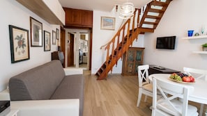 A living room with a sofa, a dining table with chairs, a staircase, and a TV mounted on the wall. - Albis 32 - Two Bedroom Apartment, Sleeps 4 (Alghero)