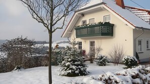 Ein Haus mit Balkon, umgeben von schneebedeckten Bäumen und Sträuchern.