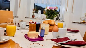 Ein Frühstückstisch mit verschiedenen Speisen, einer Blumenvase und einem Fenster mit Vorhängen.