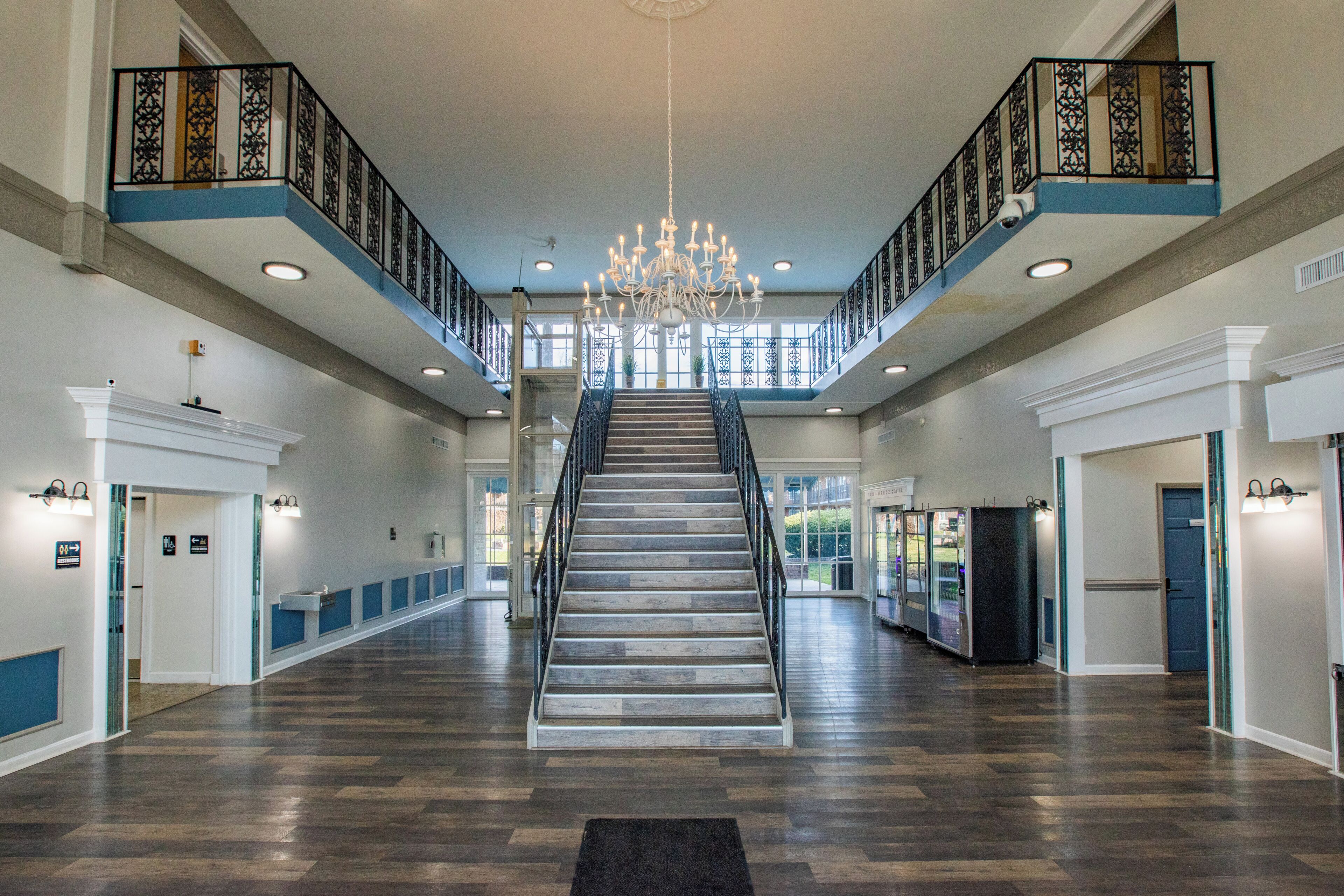 A spacious interior with a central staircase, a chandelier, and a blue railing on the upper level.