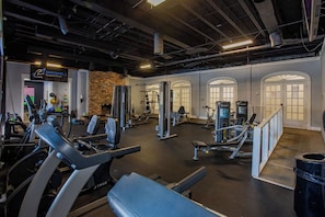Ein Fitnessstudio mit unterschiedlicher Trainingsausstattung, einer Ziegelwand und Rundbogenfenstern.