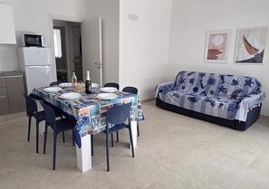 Ein Essbereich mit einem Tisch für vier Personen, einer Couch, einer Mikrowelle und einem Kühlschrank im Hintergrund.