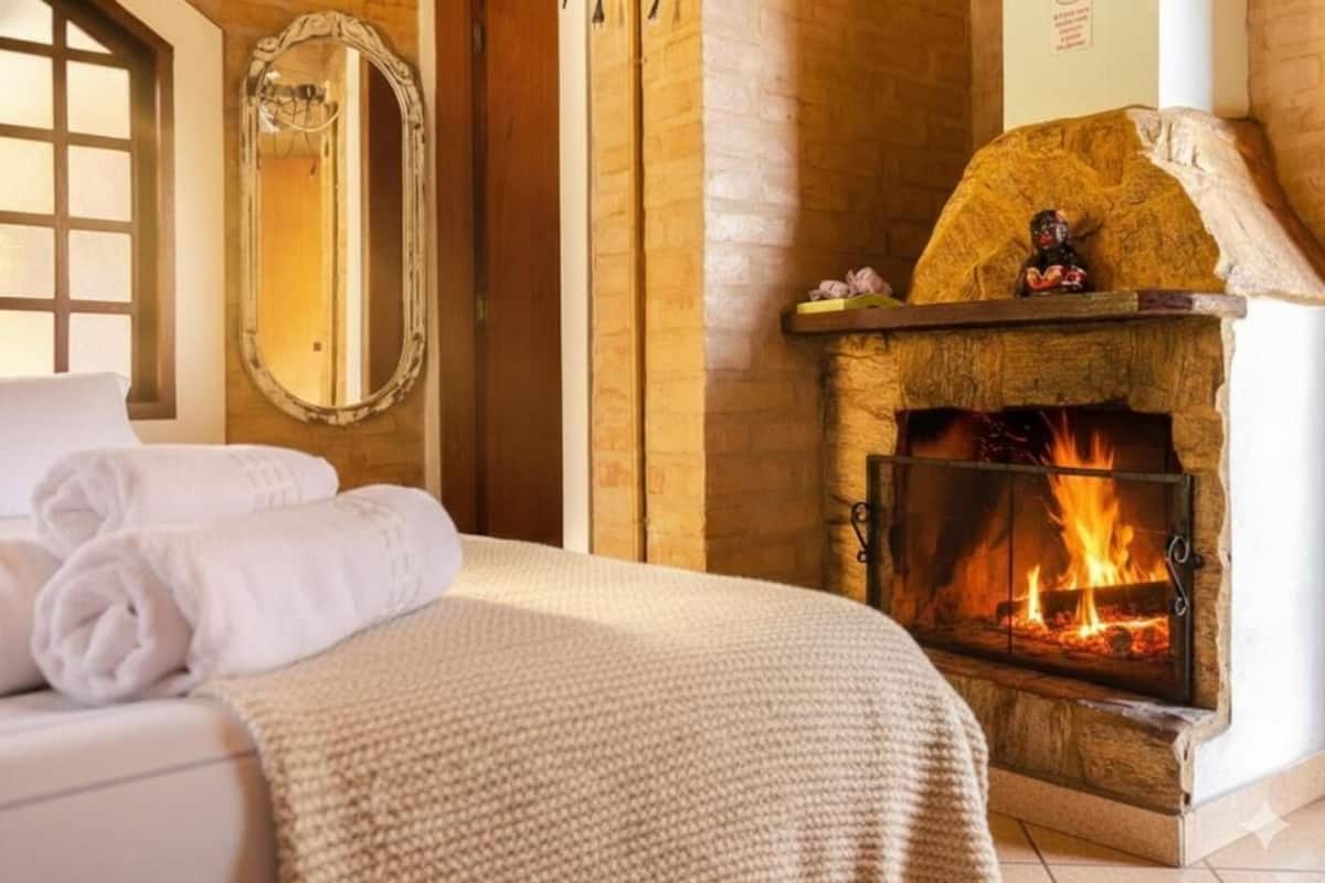 Hotellihuone, jossa on takka, valkoisilla lakanoilla varustettu sänky, peili ja ikkuna.