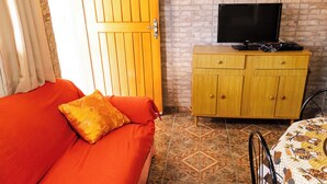 Ein Zimmer mit einer Couch, einem Fernseher auf einer Holzkommode und einer gemusterten Tischdecke.