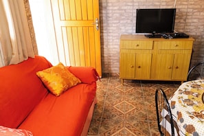 Una habitación con sofá, televisor sobre un mueble de madera y mantel con estampado.