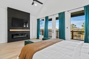 Ein Schlafzimmer mit einem Bett, einem an einer schwarzen Wand montierten Fernseher und einem Balkon mit Vorhängen.