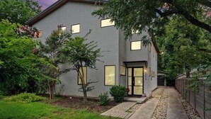 Een modern huis met twee verdiepingen, een geplaveid pad, een kleine tuin en een houten hek.