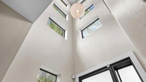 Een kamer met dakramen, een hanglamp en een raam met uitzicht op bomen.
