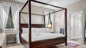 Una cama con dosel, ropa de cama blanca, una mesita de noche, una lámpara y una obra de arte enmarcada en la pared.