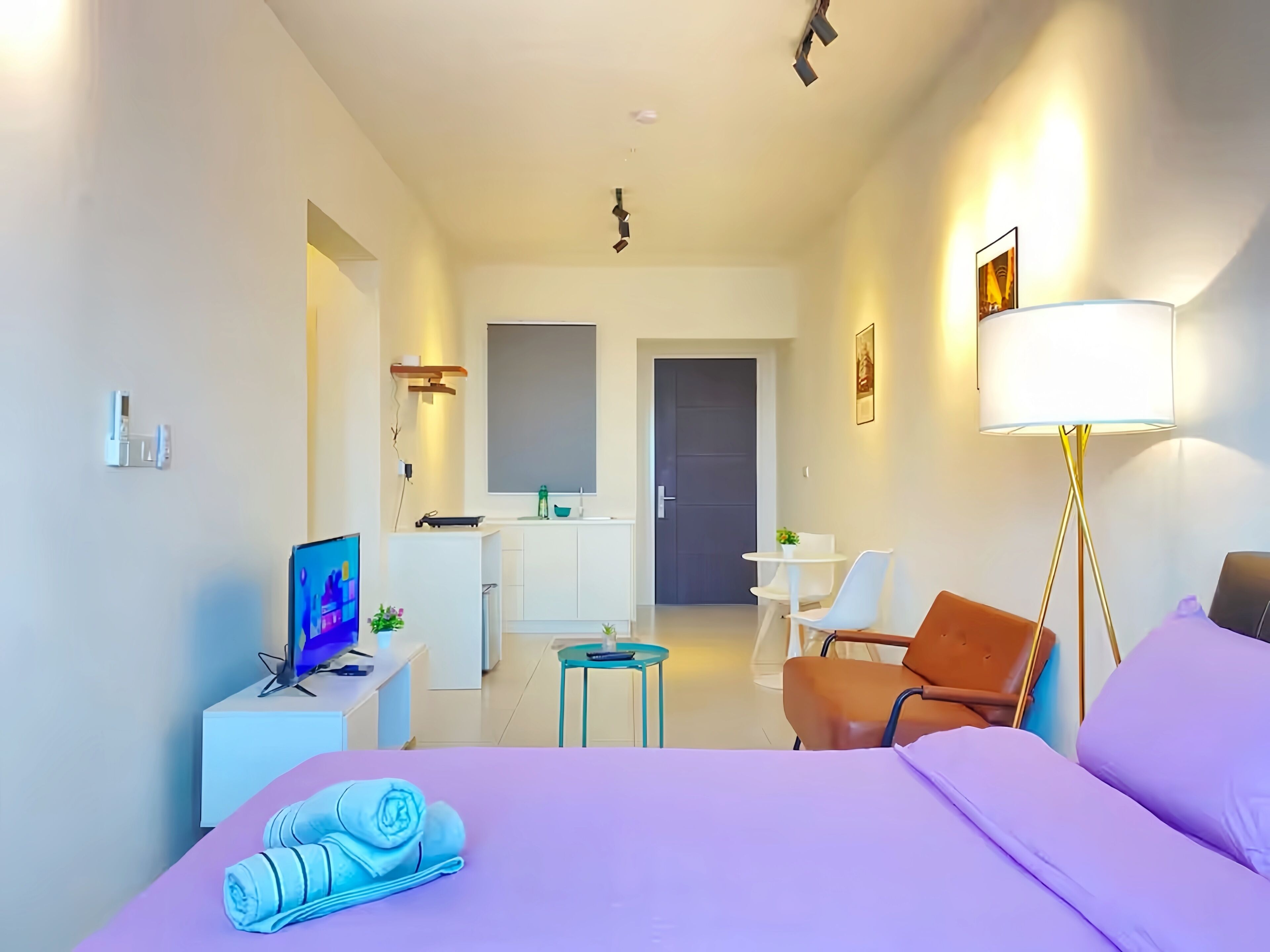A modern hotel room with a bed, a desk, a chair, a small table, and a kitchenette.