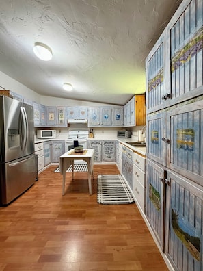A kitchen with wooden cabinets, a refrigerator, microwave, stove, and a dining table with a rug.