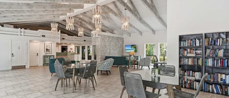 A spacious living area with a high ceiling, exposed beams, and a large bookshelf.