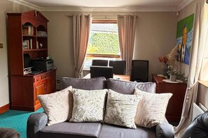 A living room with a sofa, a desk, a bookshelf, and a window with curtains. - Luxury Private Apartment Sleeps 4, Free Parking (Bective)