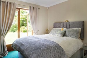 A bedroom with a bed, curtains, a nightstand, and a view of greenery outside.