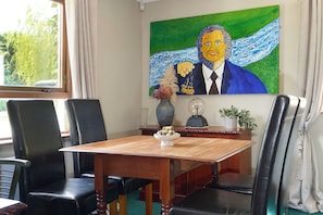 Un coin repas avec une table en bois, des chaises en cuir noir, un vase avec des fleurs, une lampe et un tableau au mur.
