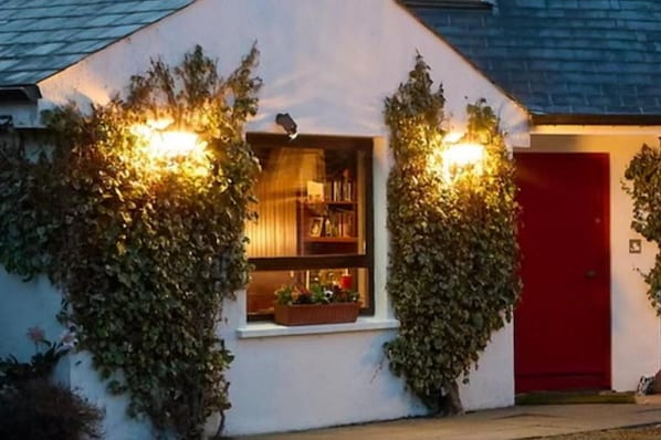 A building with ivy-covered walls, a visible window with books, and a red door.