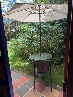 A patio area with a table and chair under a canopy, surrounded by lush greenery and flowering plants. - Family Getaway in Santa Elena (Antioquia)