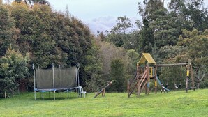 Ein Spielplatz mit Trampolin, Schaukeln und einer Kletterkonstruktion in einer grünen Wiese.