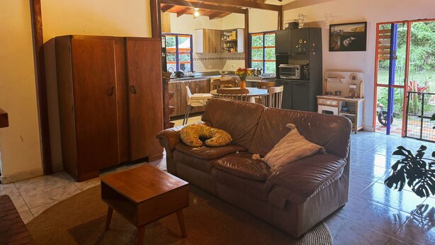 Ein gemütliches Wohnzimmer mit Ledersofa, Holzmöbeln und Blick auf die Küche und den Garten durch große Fenster.