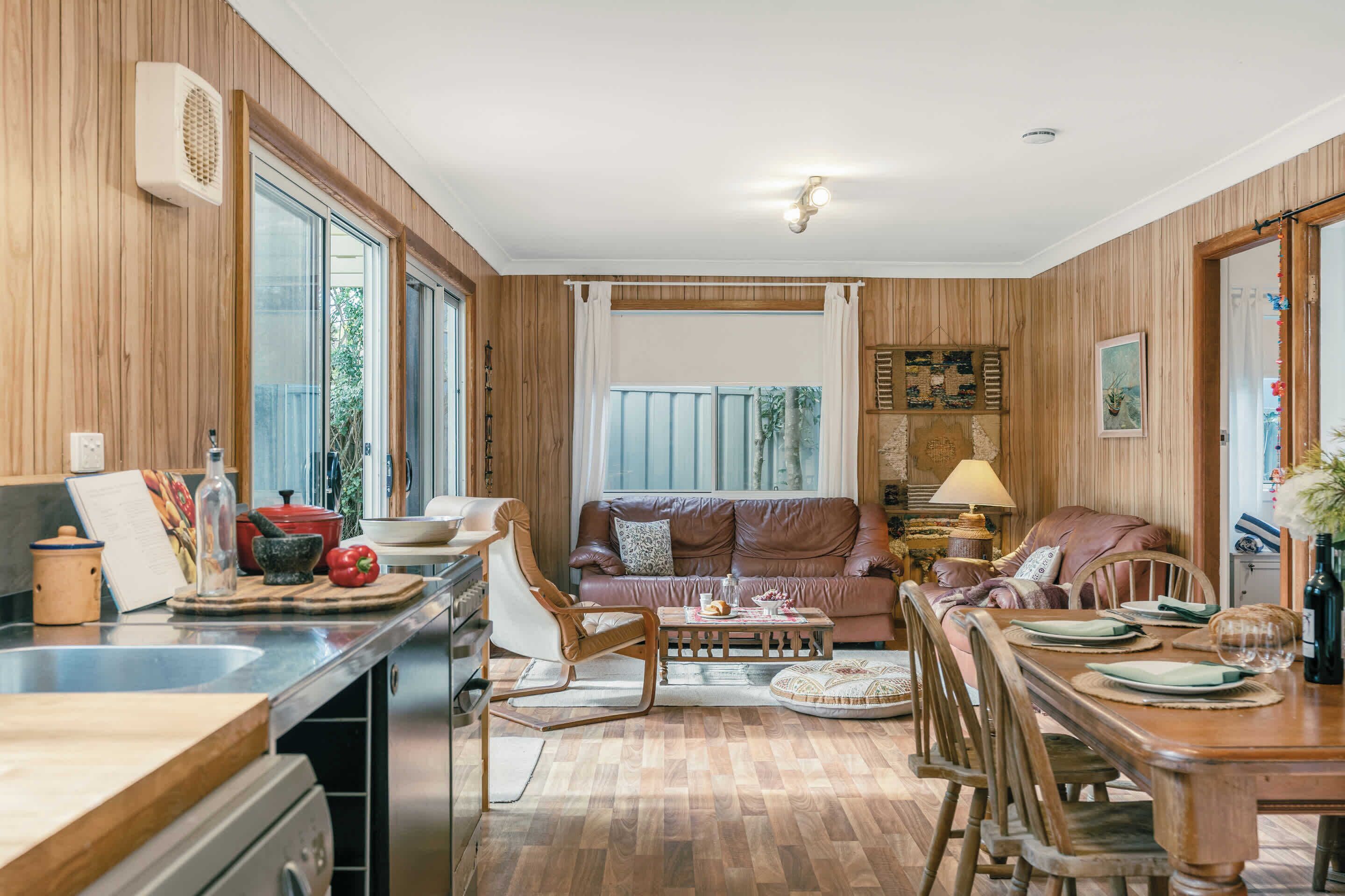 A kitchen with wooden cabinets, a dining area with a table set for two, and a living room with a sofa and a coffee table.