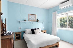 A bedroom with a bed, a window, a wall-mounted shelf with decorative items, and a wooden nightstand. - Sugar Shack Currarong (Currarong)