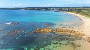 A coastal landscape with clear waters, a sandy beach, and a distant shoreline with buildings. - Sugar Shack Currarong (Currarong)
