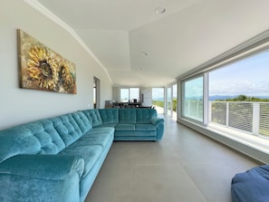 Ein geräumiger Wohnbereich mit einem großen, petrolfarbenen Ecksofa, einer Küche im Hintergrund und einem Balkon mit Blick.