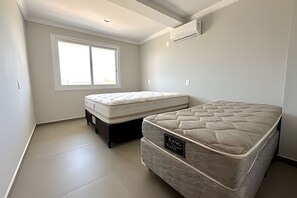 A room with two mattresses, a window, and an air conditioning unit.