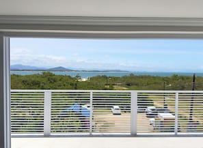 A balcony with a view of a parking area and a distant landscape including water and mountains.
