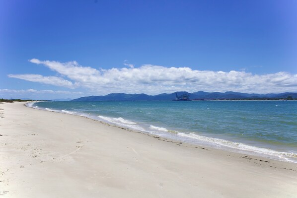 Ein Strand mit blauem Himmel, ruhigem Wasser, fernen Bergen und weiter Fernsicht.