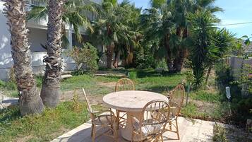 Un patio al aire libre con una mesa redonda y sillas de mimbre, rodeado de palmeras y follaje.