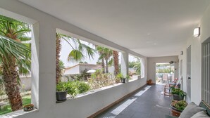 A corridor with large windows, potted plants, and a seating area with a table and chairs. - Villa 'Espectacular chalet con piscina privada y barbacoa cerca de Alicante , san juan y el Campello' (Alicante (Alacant))