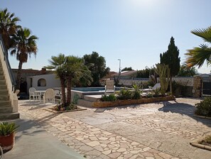 Un patio con piscina, mobiliario exterior, palmeras y un patio de piedra.