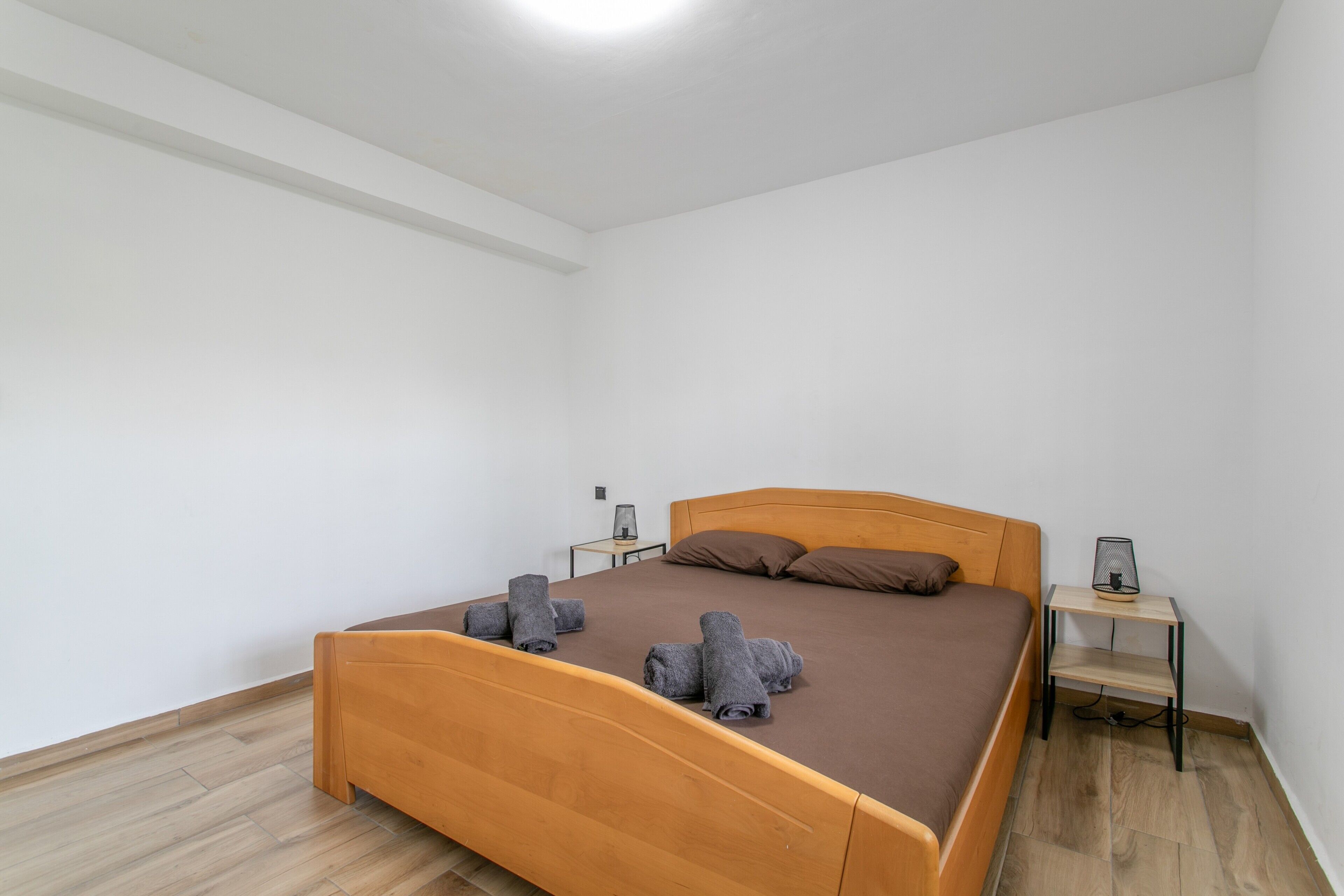A single bed with a wooden headboard, two bedside tables, and a pair of brown pillows.