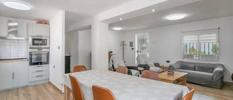 Una cocina moderna con electrodomésticos integrados, un comedor con mesa y sillas, y una sala de estar con sofá y ventana.