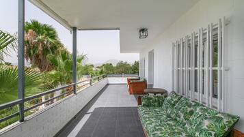 Un balcon abrité avec un coin salon, une vue sur des palmiers et un mur blanc agrémenté de fenêtres.