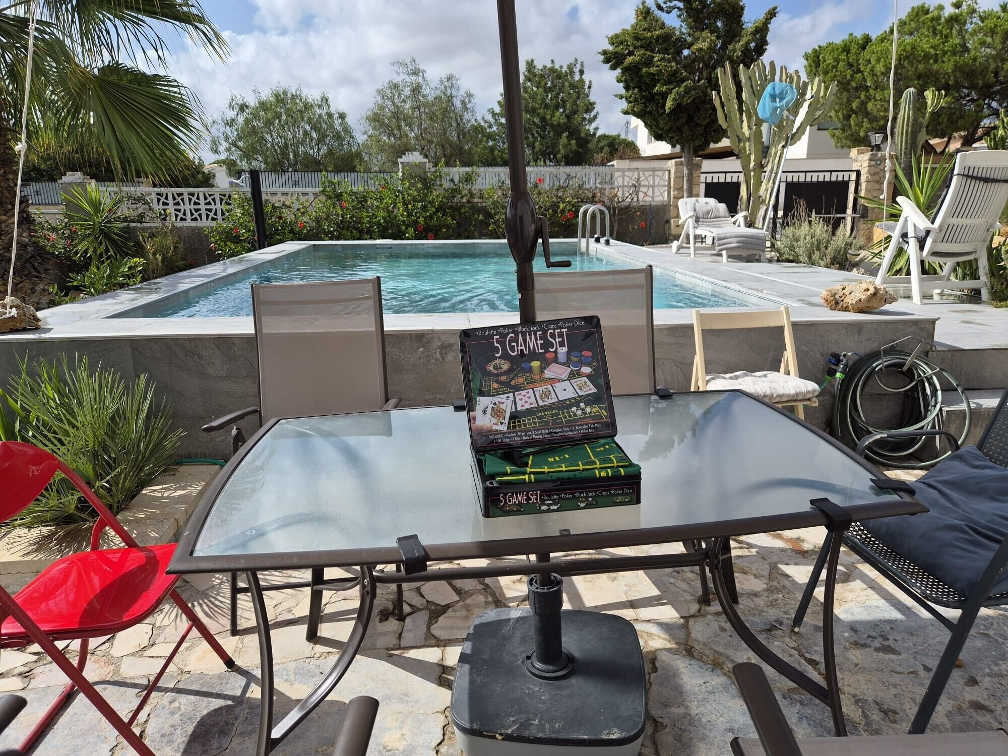 A poolside area with a table displaying a 5 game set, chairs, and a pool.
