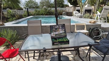 Zona de piscina con una mesa mostrando un juego de 5 piezas, sillas y una piscina.