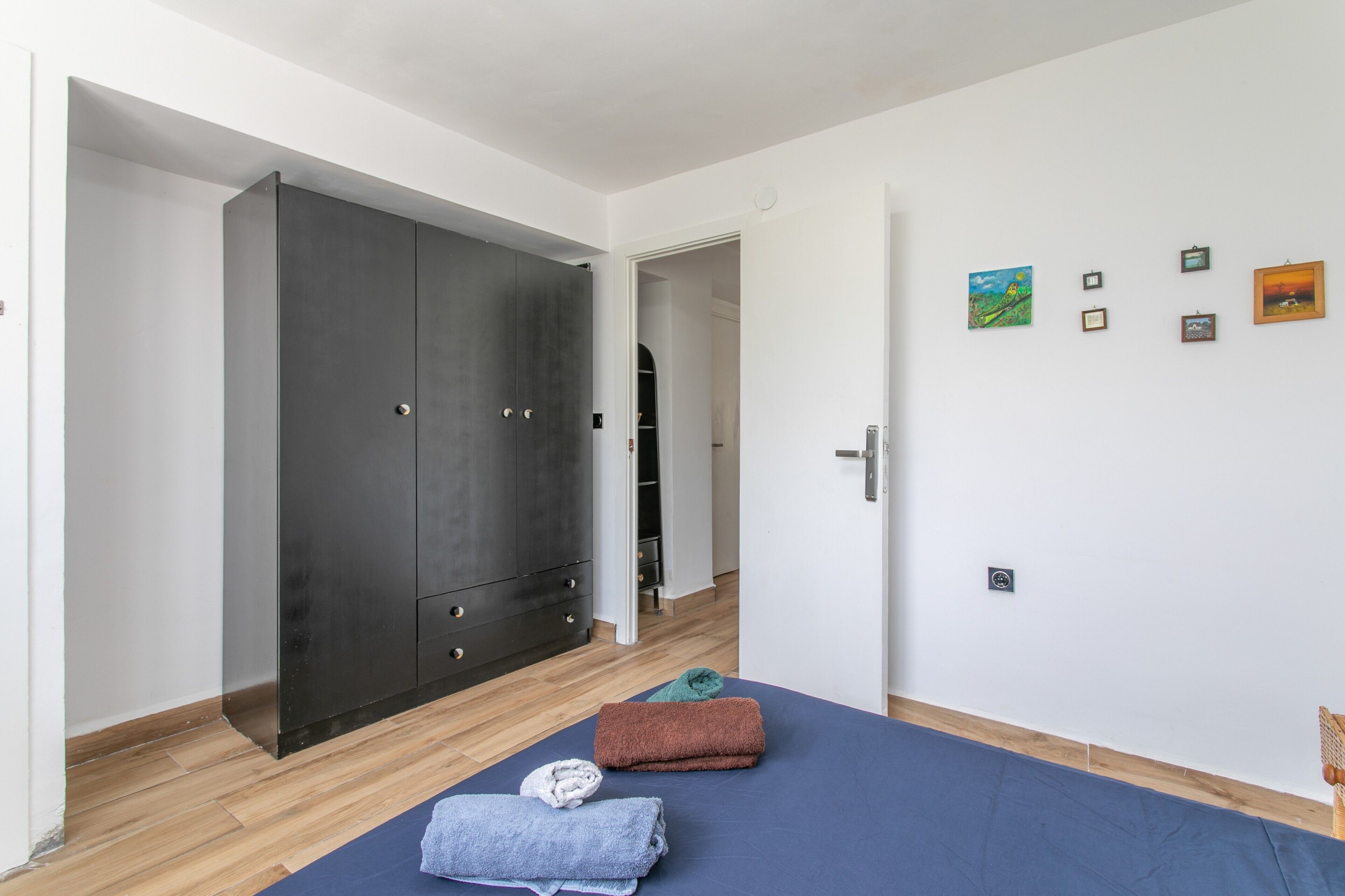 Een kamer met een grote kast, een bed met handdoeken, en een wand met ingelijste foto's.