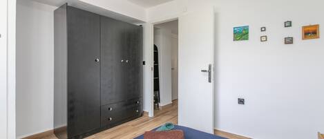 A room with a large wardrobe, a bed with towels, and a wall with framed pictures.