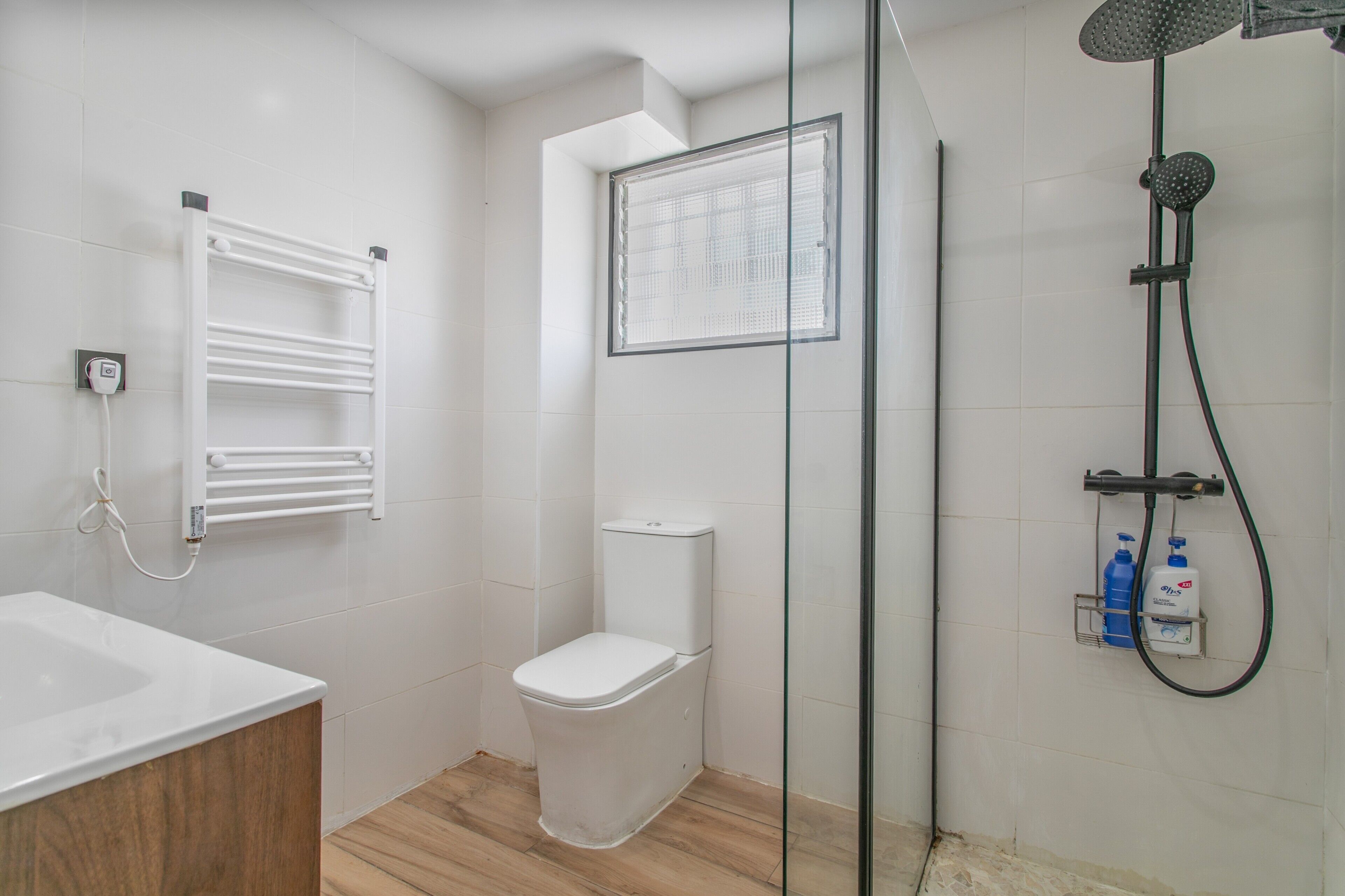 Een badkamer met toilet, douchecabine van glas, een witte wastafel en een handdoekhouder.
