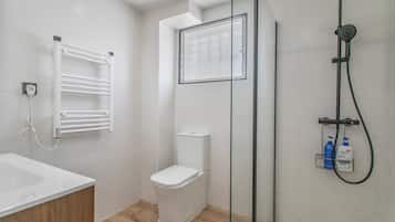 Een badkamer met toilet, douchecabine van glas, een witte wastafel en een handdoekhouder.