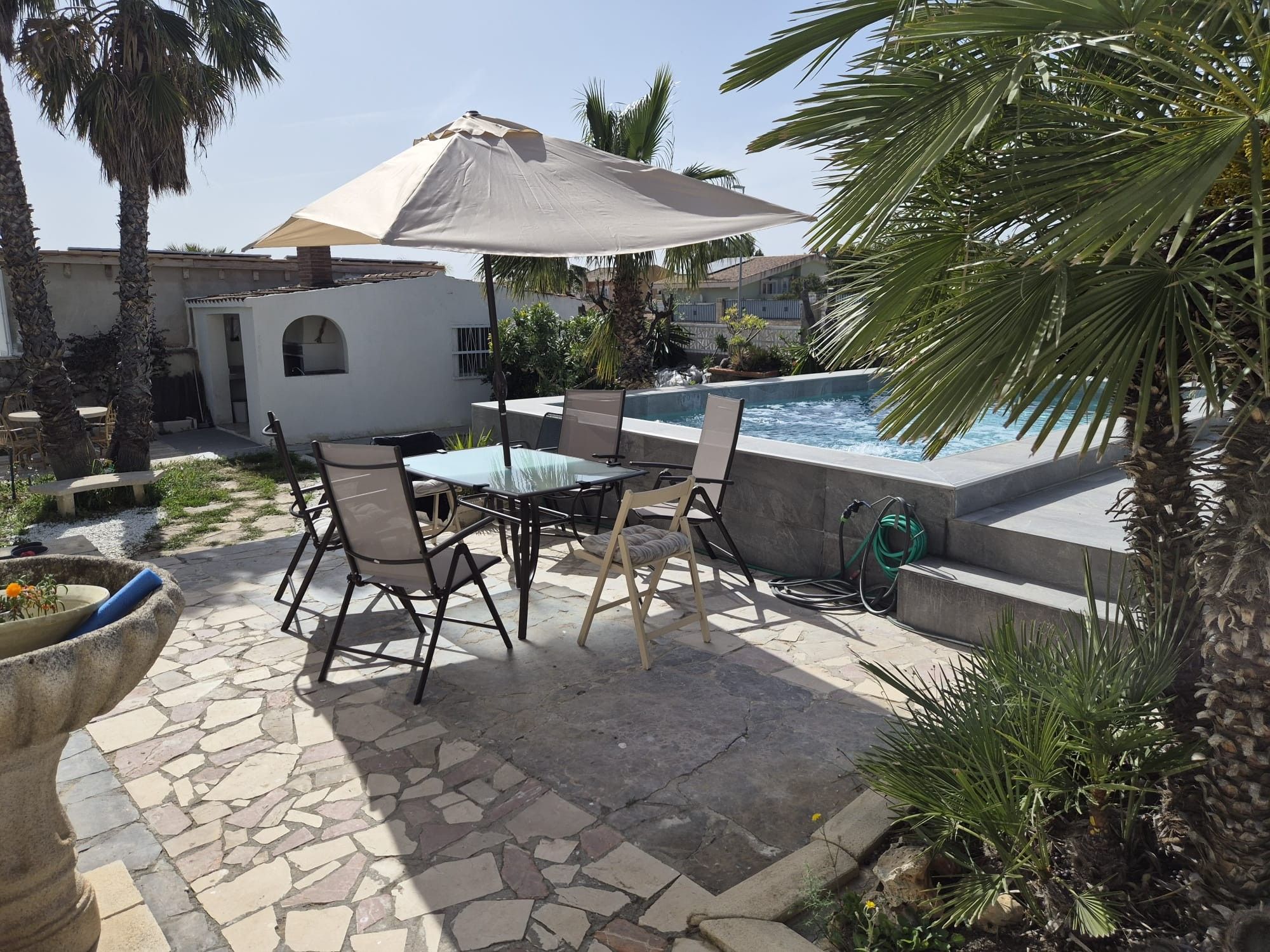 Un patio al aire libre con piscina, suelo de piedra y mobiliario exterior.