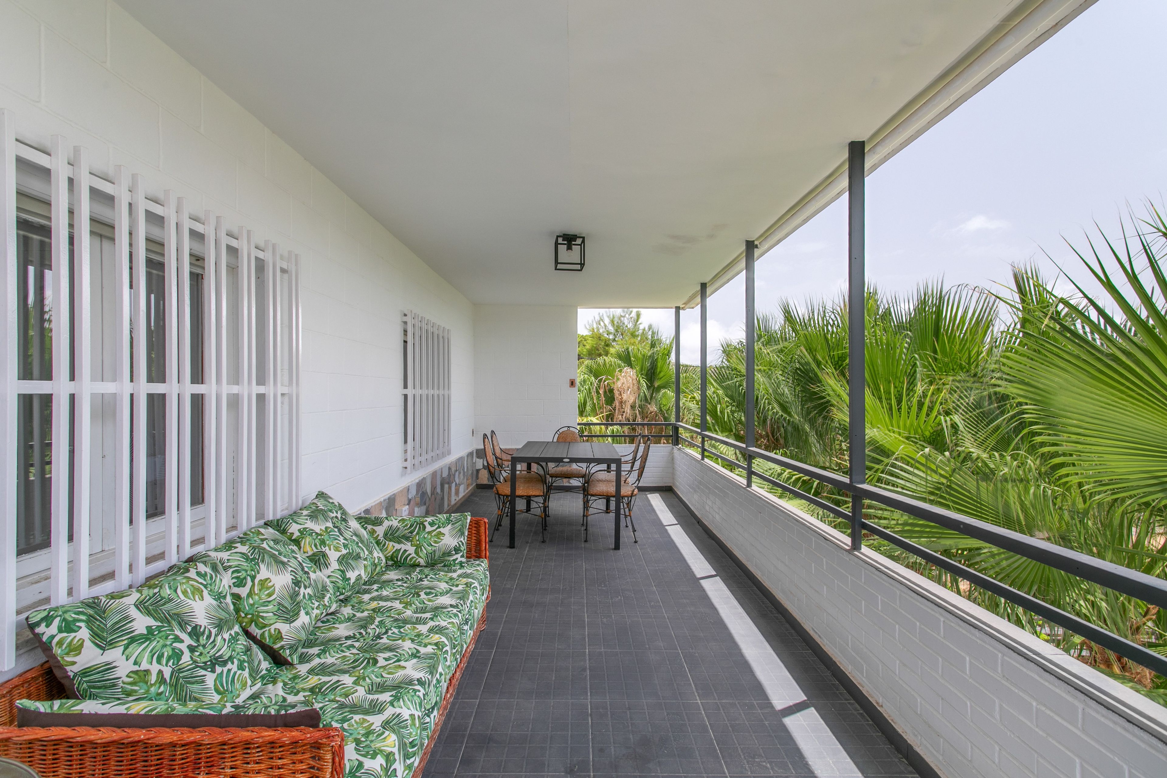 Un balcón cubierto con una mesa y sillas de comedor, un sofá con estampado tropical y vistas a la vegetación.