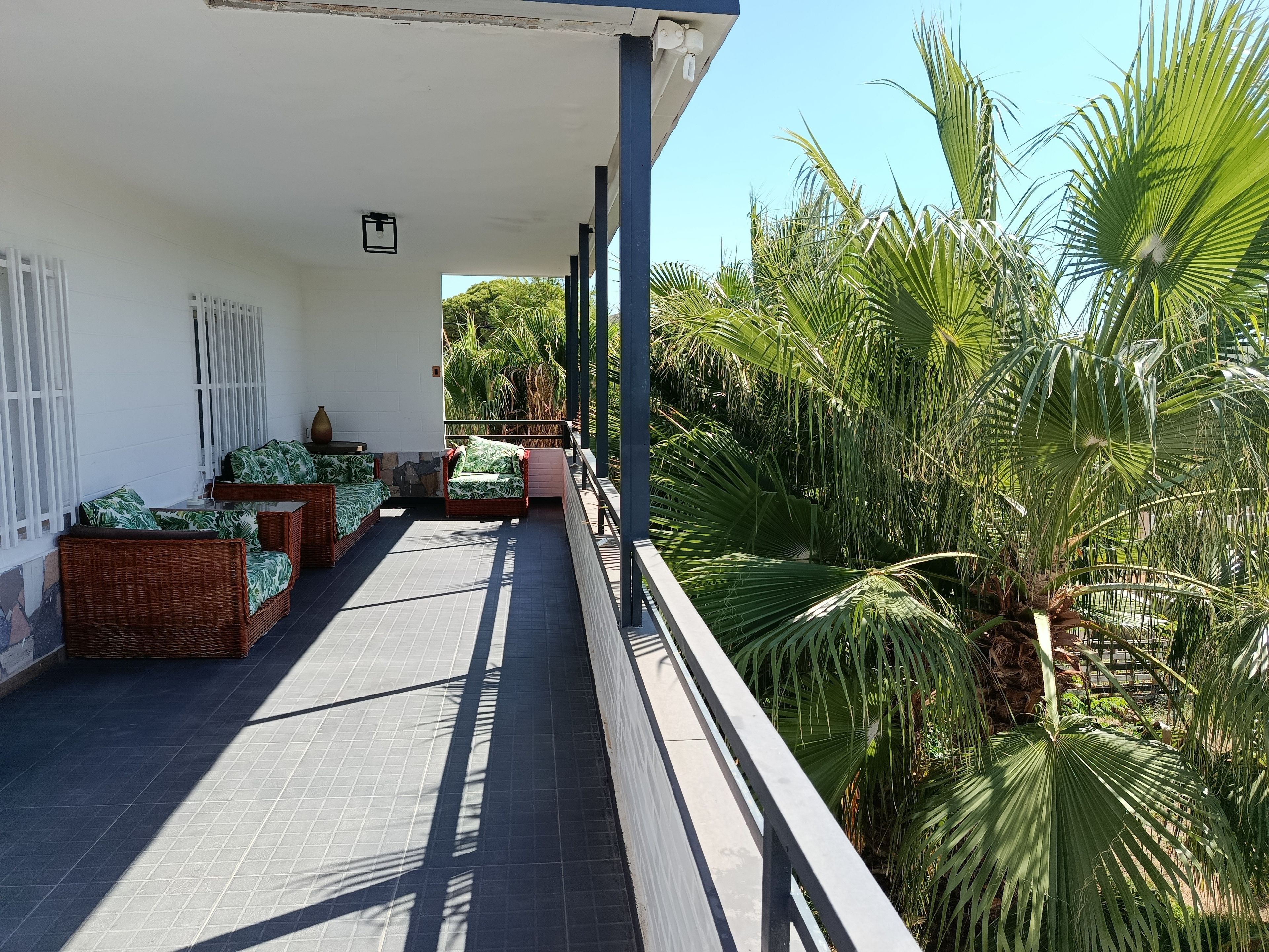 A covered outdoor area with wicker furniture and a view of tropical plants.