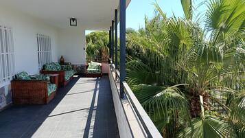 A covered outdoor area with wicker furniture and a view of tropical plants.